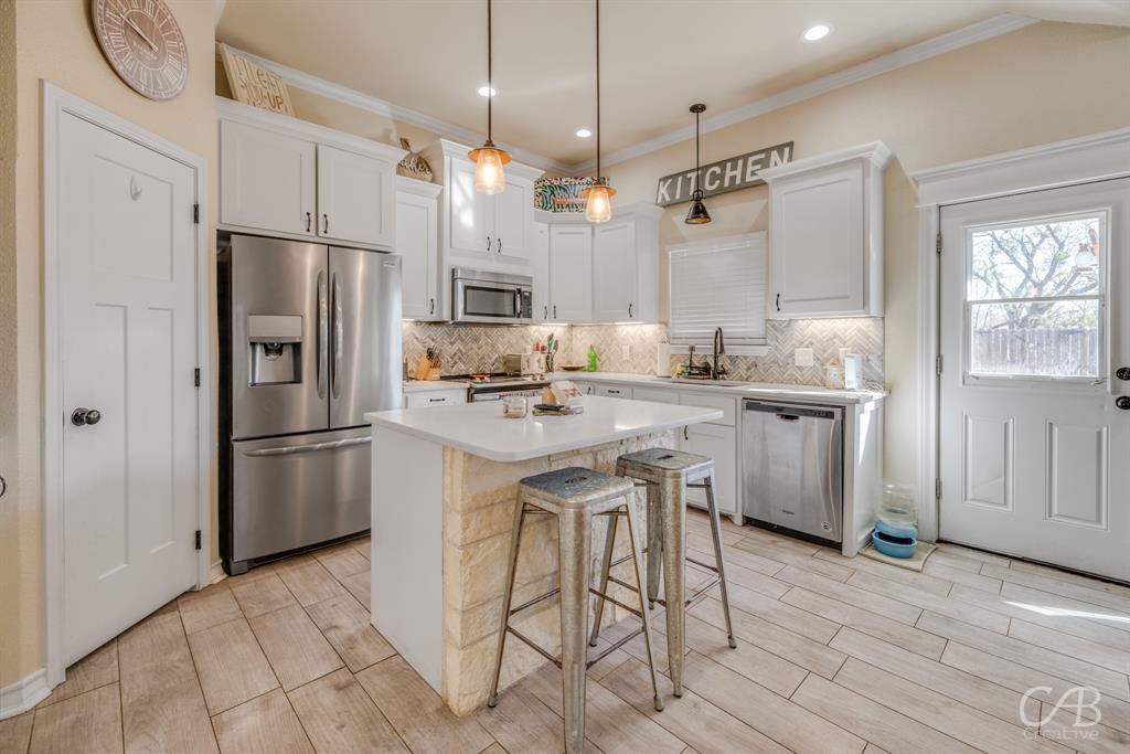 625 Jarrell Court Tuscola, TX 79562 - Photo 9 of 32 a kitchen with kitchen island a refrigerator a sink dishwasher a stove and white cabinets with wooden floor