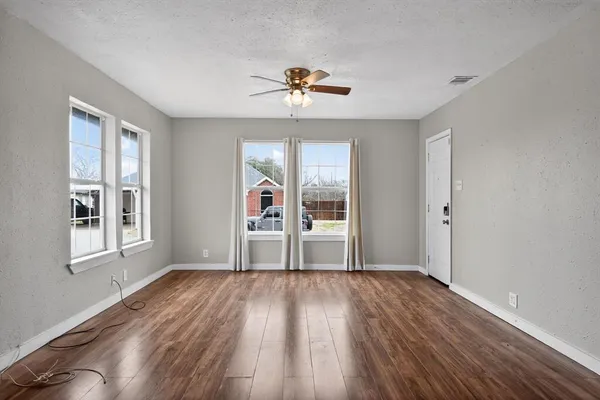 a view of an empty room with wooden floor and a ceiling fan