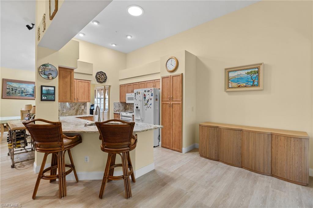 1665 Winding Oaks Way, Unit 202 Naples, FL 34109 - Photo 14 of 34 Kitchen featuring a peninsula, light wood-style floors, light stone counters, white appliances, and a breakfast bar