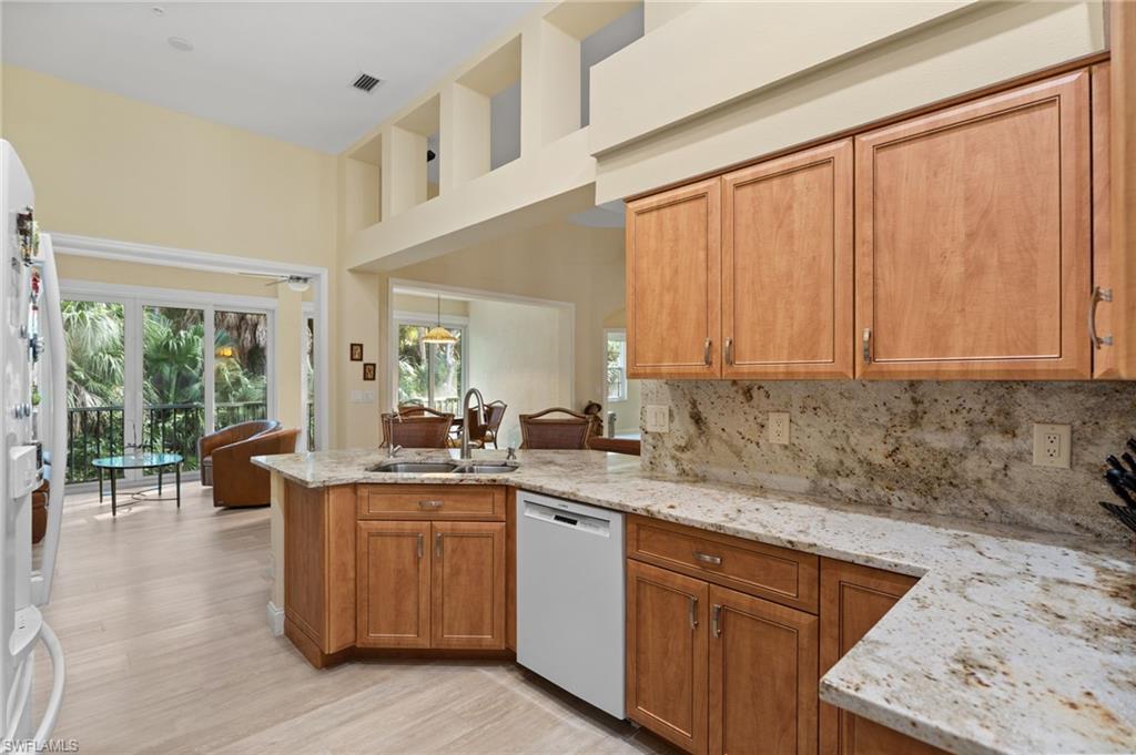 1665 Winding Oaks Way, Unit 202 Naples, FL 34109 - Photo 18 of 34 Kitchen with light stone counters, wood finish cabinets, dishwasher, decorative backsplash, and light wood-style flooring