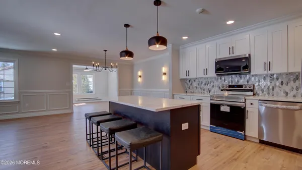 a kitchen with stainless steel appliances granite countertop a stove a sink a microwave a refrigerator and white cabinets with wooden floor