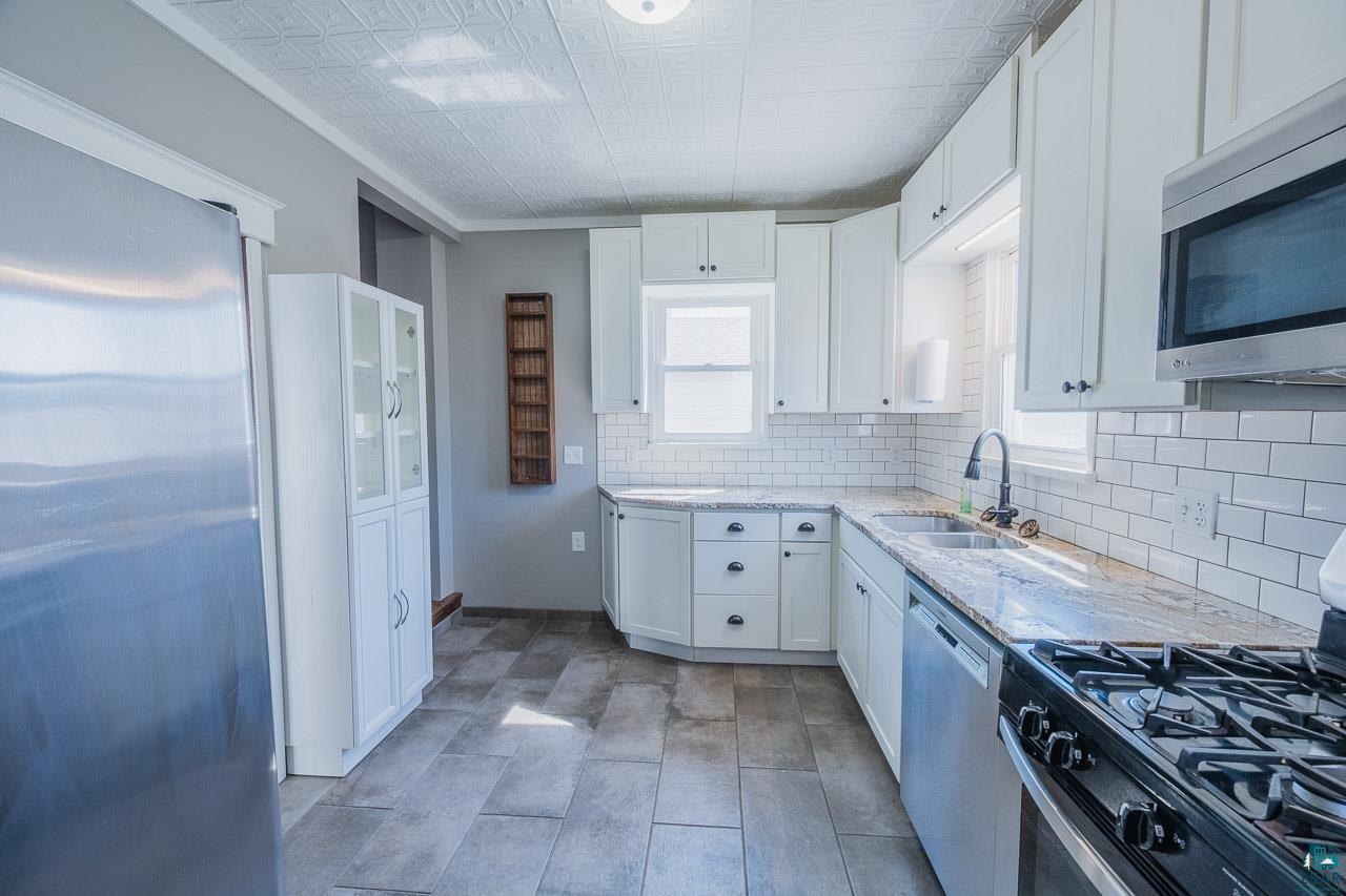 508 10th Street South Virginia, MN 55792 - Photo 11 of 43 Modern kitchen featuring white cabinetry, granite countertops, subway tile backsplash, and stainless steel appliances