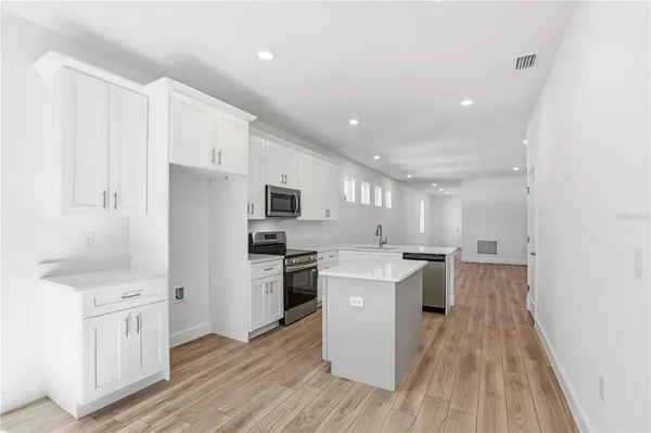 a kitchen with stainless steel appliances a refrigerator stove a sink and white cabinets with wooden floor