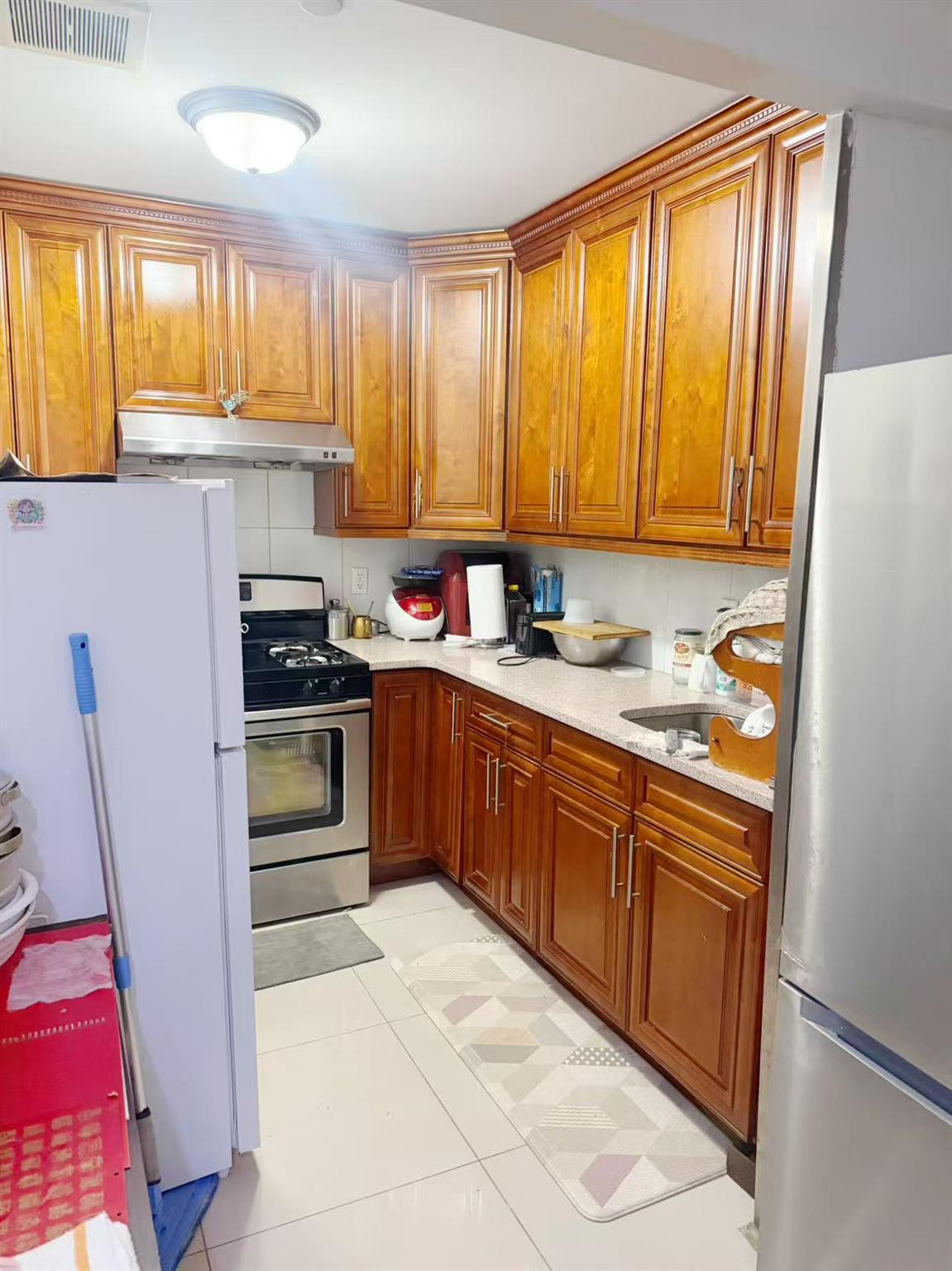 108-31 50th Avenue, Unit 3A Queens, NY 11368 - Photo 7 of 7 Kitchen with appliances with stainless steel finishes, brown cabinetry, under cabinet range hood, and light tile patterned floors
