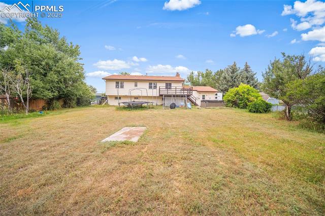 1921 Wooten Road Colorado Springs, CO 80915 - Photo 34 of 49 Rear view of house featuring a wooden deck, stairs, a chimney, and a trampoline