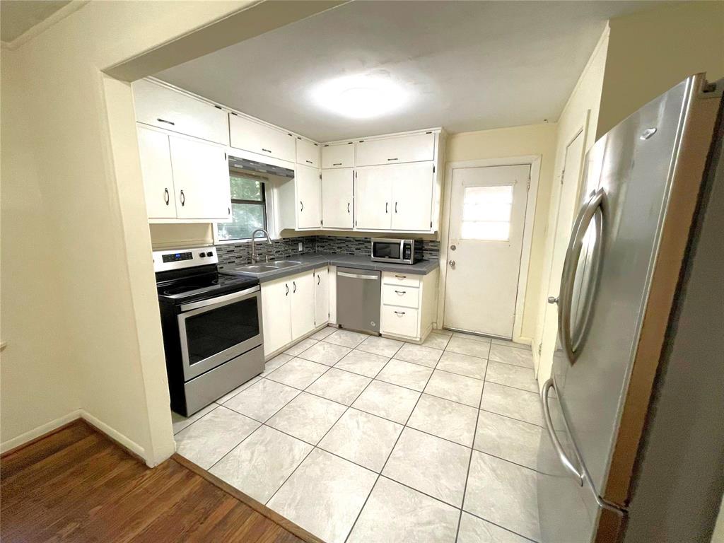 501 South Perry Avenue Denison, TX 75020 - Photo 4 of 11 Kitchen featuring white cabinetry, stainless steel appliances, tile flooring, a window, and a door with a window pane