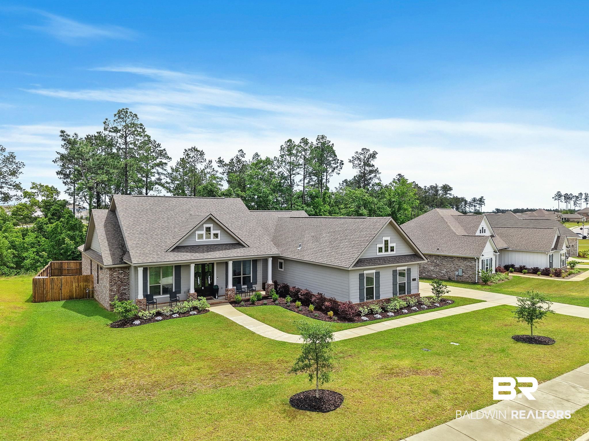 13233 Ibis Boulevard Daphne, AL 36527 - Photo 68 of 100 Contemporary residence featuring a light gray exterior with stone accents, a covered front porch, a gabled roofline, a manicured lawn, and perimeter landscaping