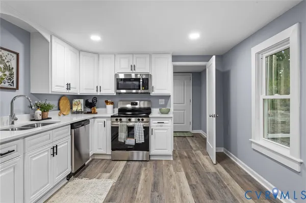 a kitchen with stainless steel appliances granite countertop a stove top oven a sink dishwasher and a refrigerator with wooden floor