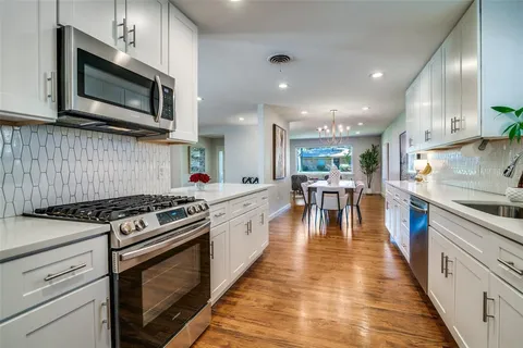 a kitchen with stainless steel appliances granite countertop a stove top oven a sink dishwasher a dining table and chairs with wooden floor