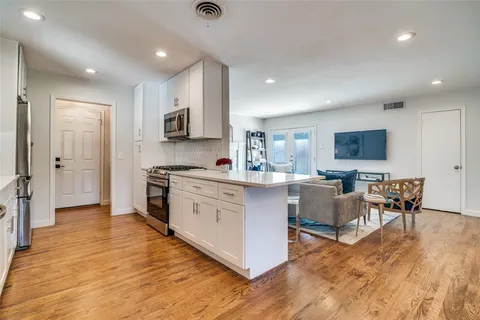 a kitchen with stainless steel appliances granite countertop a stove top oven a sink dishwasher a refrigerator and white cabinets with wooden floor