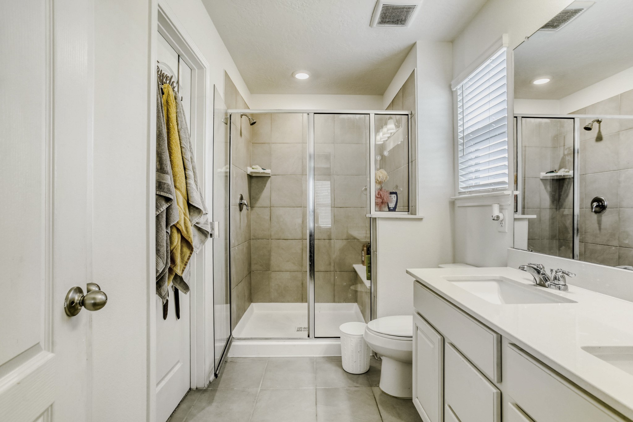 3331 Forest Chitto Dr Spring Spring, TX 77373 - Photo 18 of 29 This primary bathroom features a modern design with a spacious glass-enclosed shower, a sleek white vanity with ample storage, and a large mirror. Natural light flows in through a window with blinds, enhancing the clean, bright atmosphere.