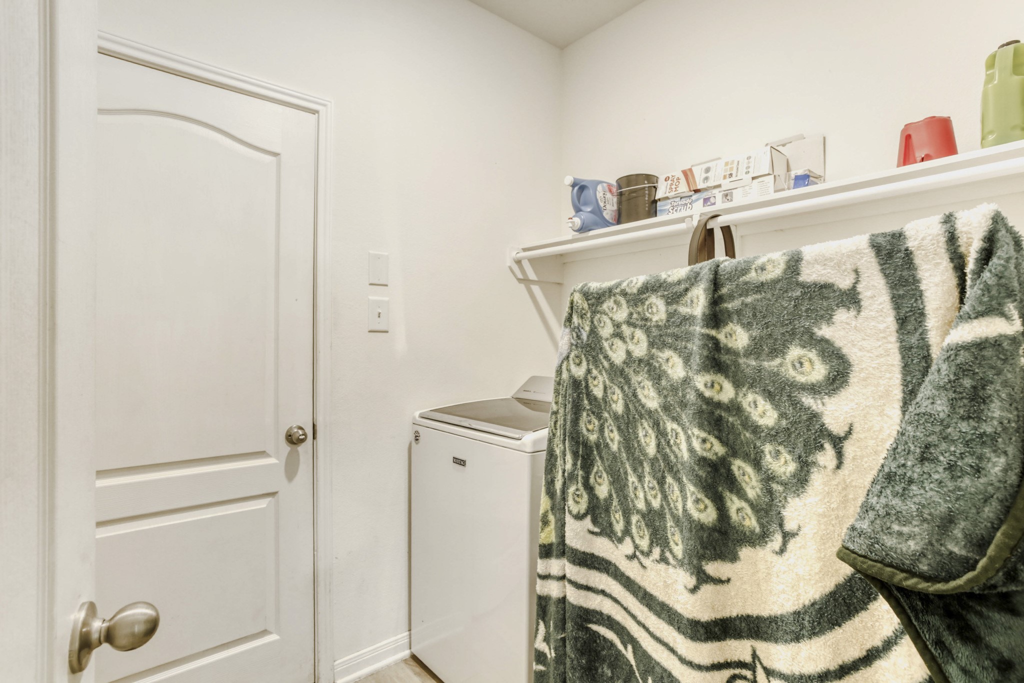3331 Forest Chitto Dr Spring Spring, TX 77373 - Photo 26 of 29 This photo shows a compact laundry room with a washing machine, shelves for storage, and a door leading to the garage. The space is functional and organized, ideal for efficient laundry tasks.