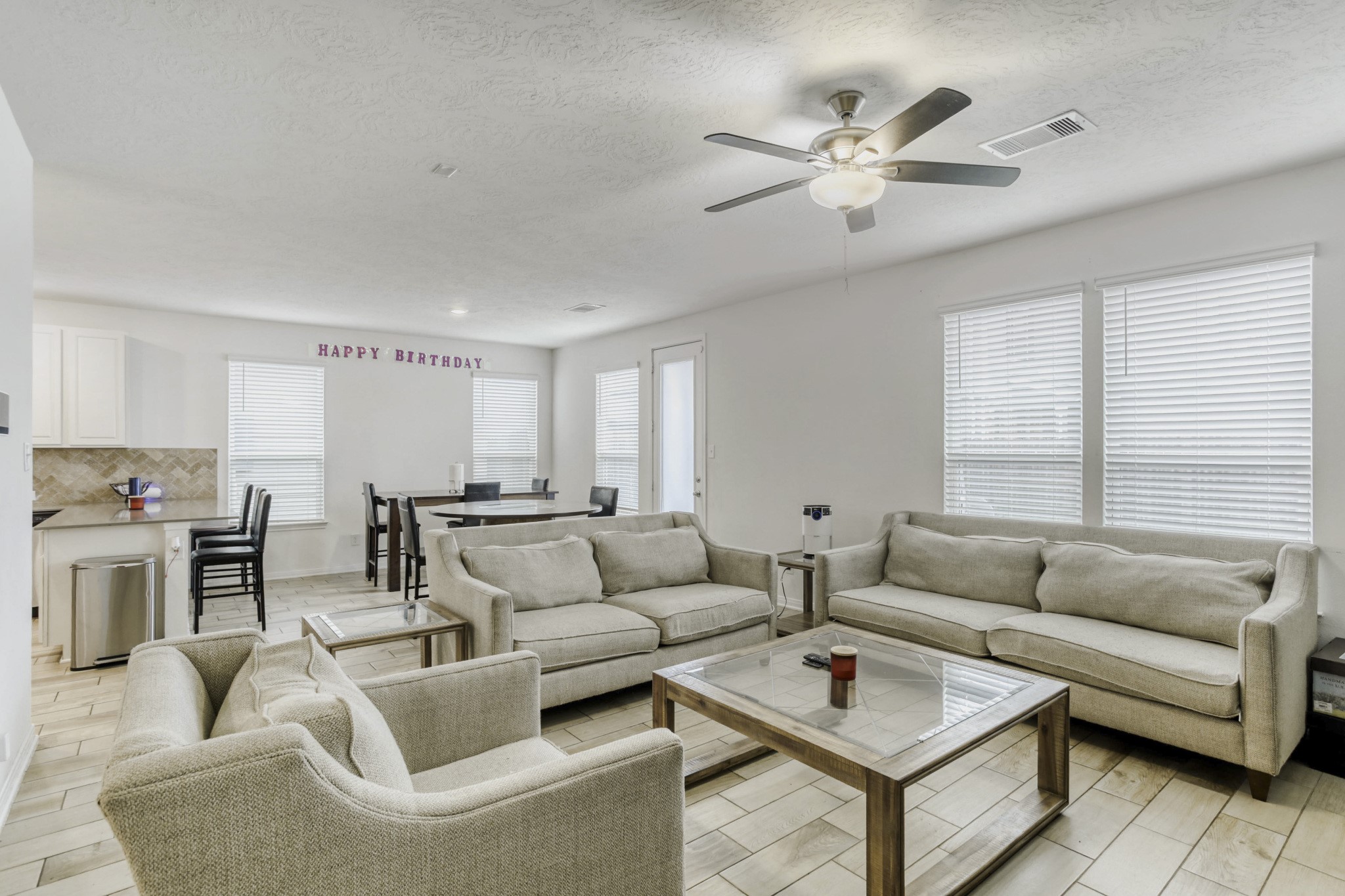 3331 Forest Chitto Dr Spring Spring, TX 77373 - Photo 7 of 29 This photo showcases a the bright living area with a ceiling fan, and natural light streaming through large windows. The open layout seamlessly connects to a dining space and kitchen, creating an inviting and functional living environment.