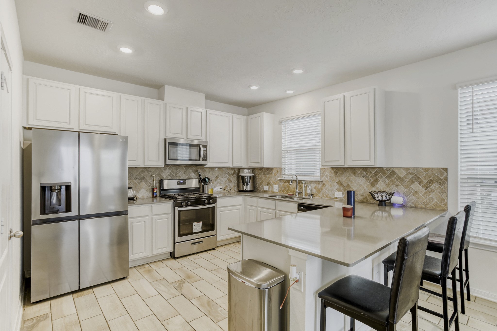 3331 Forest Chitto Dr Spring Spring, TX 77373 - Photo 9 of 29 Modern kitchen with stainless steel gas appliances, light tile flooring, and ample white cabinetry. Features a spacious countertop with bar seating and stylish tile backsplash. Bright and inviting with recessed lighting.
