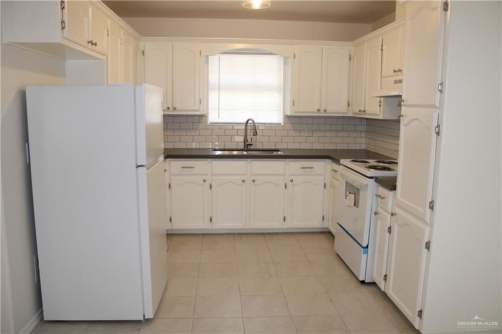 1408 Pine Street, Unit D Weslaco, TX 78596 - Photo 3 of 10 Kitchen with white appliances, dark countertops, decorative backsplash, and white cabinets