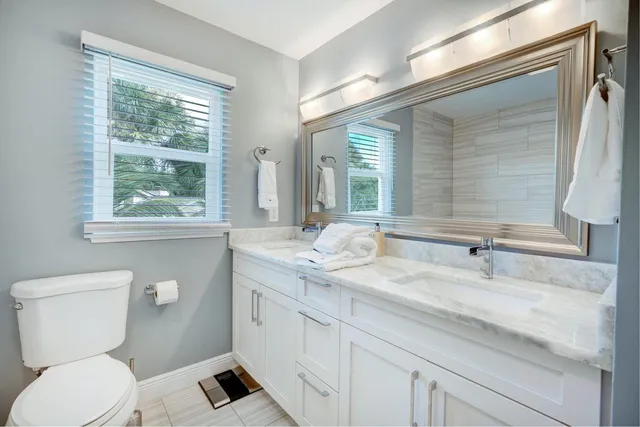 a bathroom with a granite countertop sink toilet a large mirror a bathtub and next to a window