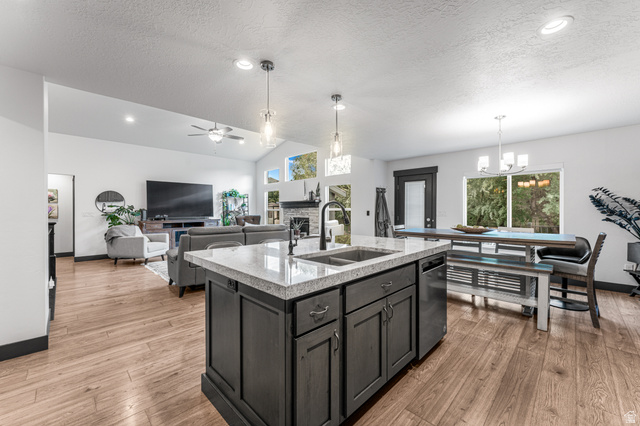 313 Old Maple Road South Weber, UT 84405 - Photo 12 of 35 Open-concept interior featuring wood-finish flooring, a kitchen island with stone countertops and an undermount sink, recessed lighting, and vaulted ceilings