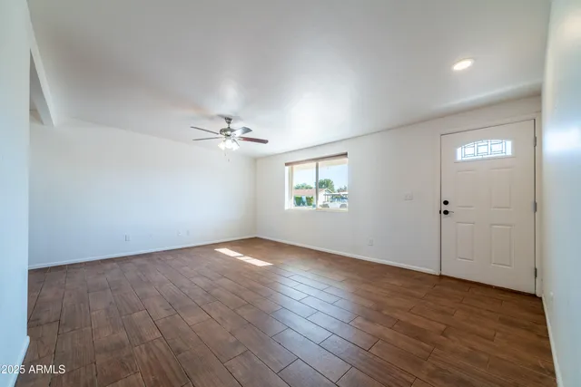 an empty room with wooden floor chandelier fan and windows