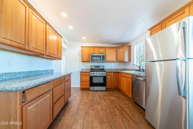 a kitchen with stainless steel appliances granite countertop a refrigerator a stove top oven a sink and dishwasher with wooden floor