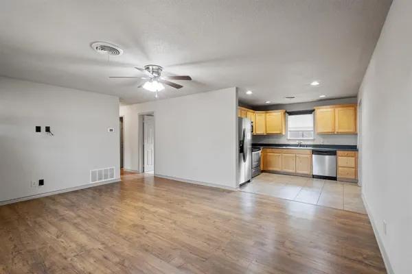 an empty room with wooden floor and a kitchen