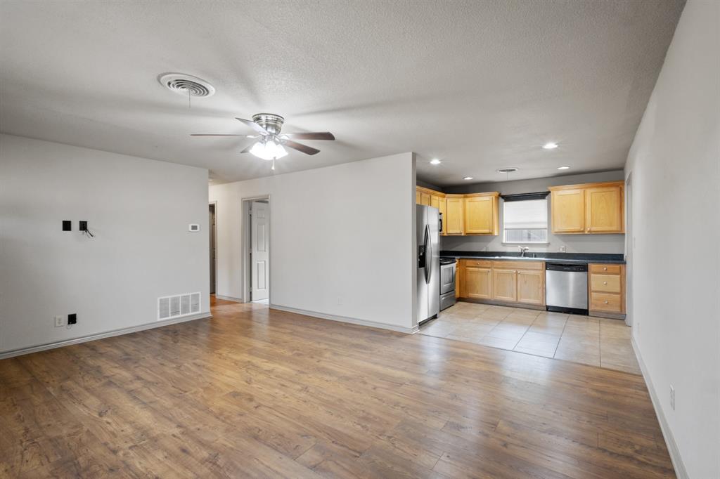 1004 North Cates Street Decatur, TX 76234 - Photo 3 of 30 an empty room with wooden floor and a kitchen