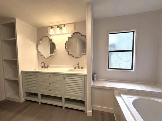a bathroom with a double vanity sink and mirror with bathtub
