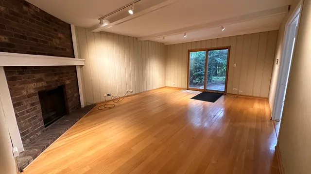 a view of an empty room with wooden floor fireplace and a window