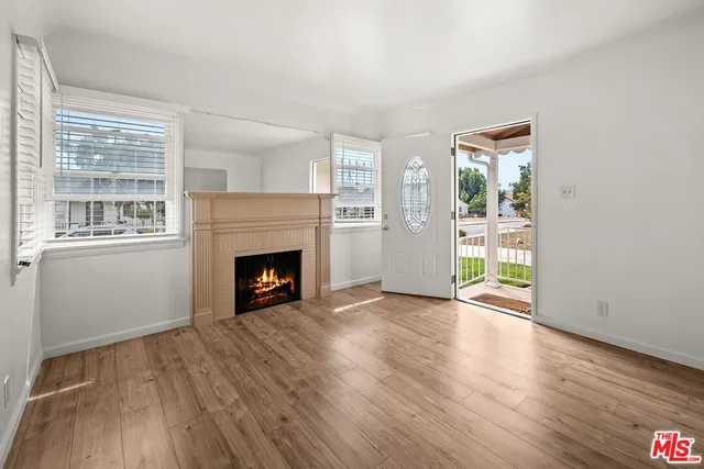 a view of an empty room with wooden floor fireplace and a window