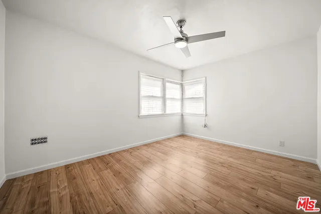 an empty room with wooden floor fan and windows