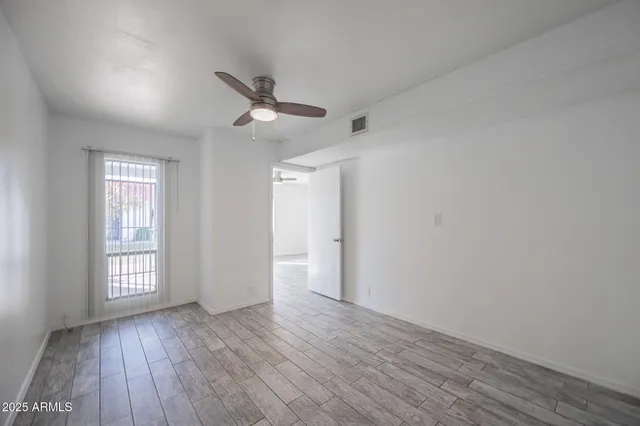 an empty room with wooden floor ceiling fan and windows
