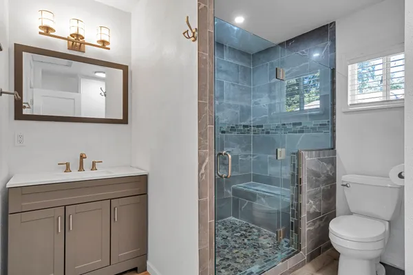 a bathroom with a granite countertop toilet a sink a mirror and shower