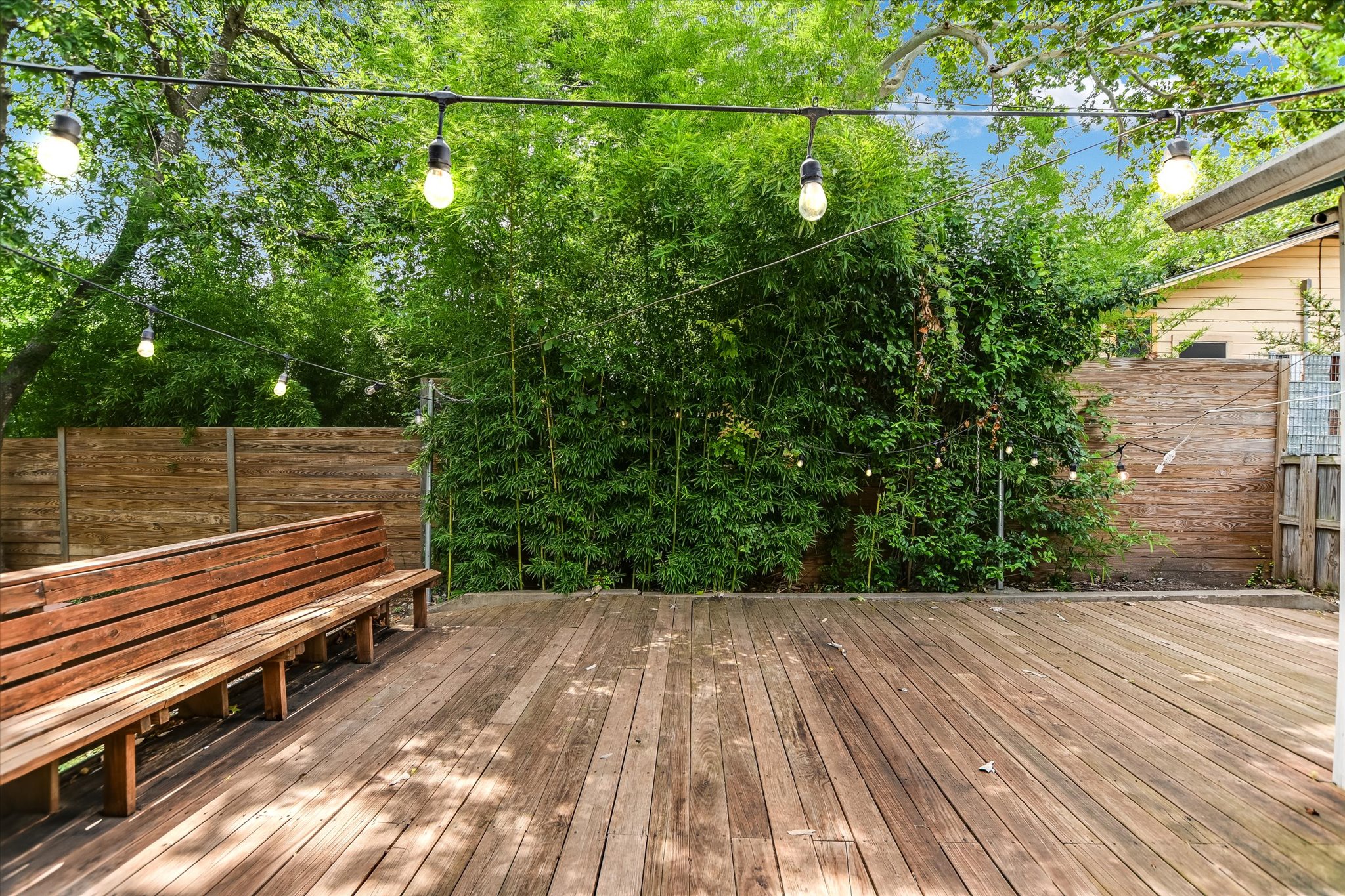 208 Braeswood Road Austin, TX 78704 - Photo 17 of 20 A spacious wooden deck provides an inviting outdoor entertainment area, complemented by string lights and lush greenery.