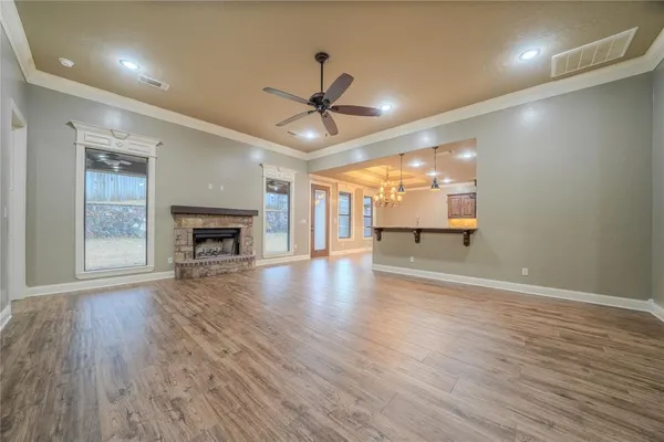 an empty room with wooden floor a ceiling fan a kitchen view and a fireplace