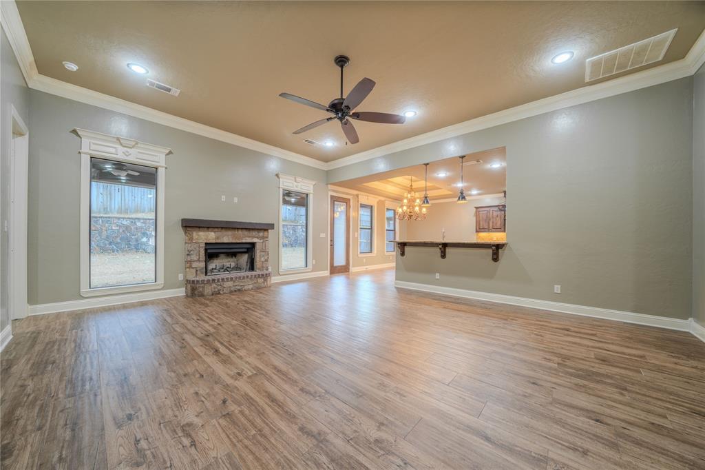 2114 West Hawkins Parkway Longview, TX 75605 - Photo 5 of 27 an empty room with wooden floor a ceiling fan a kitchen view and a fireplace