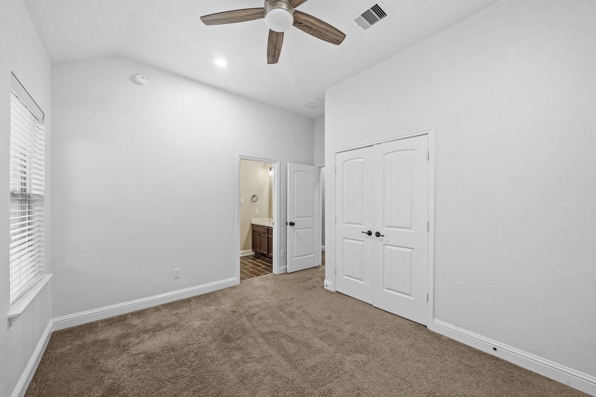 14215 Spindle Arbor Road Cypress, TX 77429 - Photo 26 of 47 This photo showcases a bright, empty room with neutral walls and carpet, featuring a ceiling fan and plenty of natural light. There is a double door closet and an open doorway leading to a bathroom.