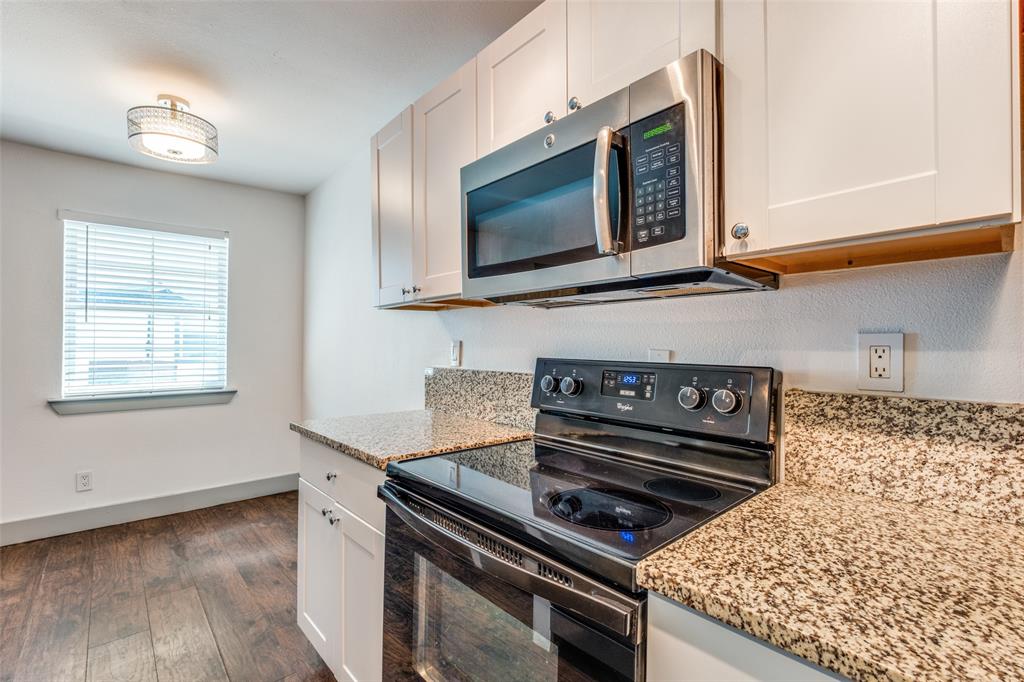 4633 Fairmount Street, Unit 109 Dallas, TX 75219 - Photo 11 of 14 Kitchen featuring granite countertops, a black electric range, stainless steel microwave, white shaker-style cabinetry, and wood-finish flooring