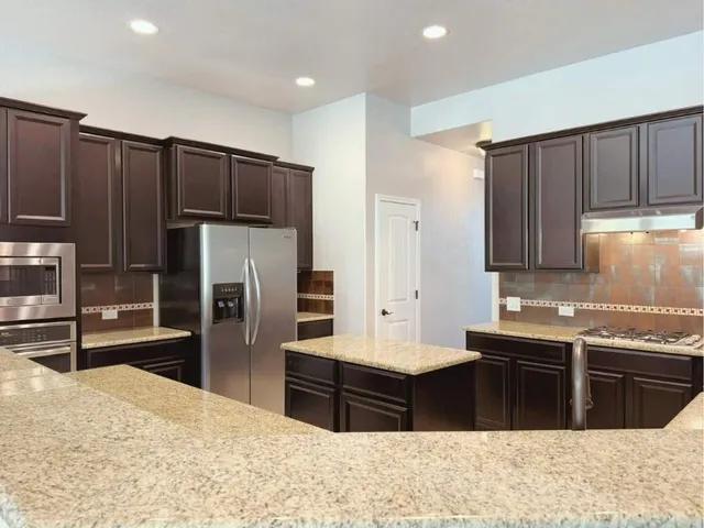 a kitchen with stainless steel appliances kitchen island granite countertop a refrigerator and a sink