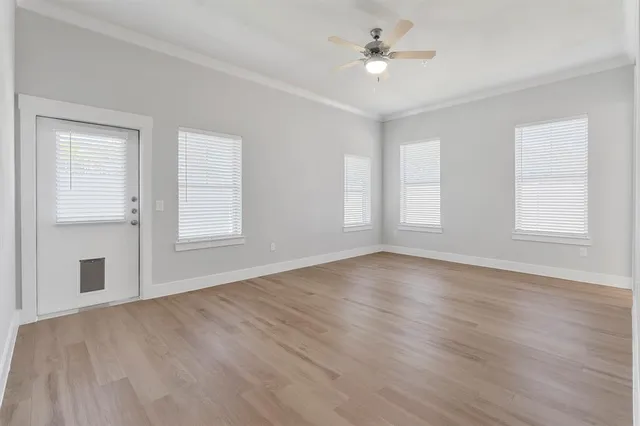 an empty room with wooden floor ceiling fan and windows