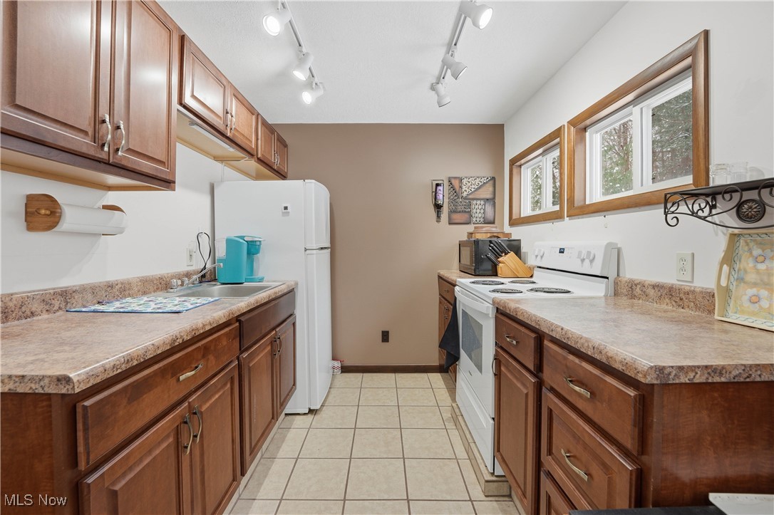 4254 Doral Road Southwest Carrollton, OH 44615 - Photo 25 of 46 Kitchen featuring white appliances, track lighting, brown cabinets, light tile patterned floors, and light countertops