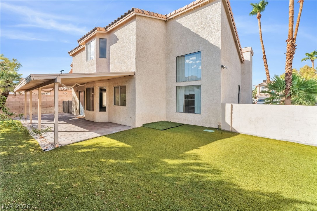 1402 Rim Fire Circle Henderson, NV 89014 - Photo 42 of 48 An inviting covered patio overlooks a grassy backyard enclosed by a solid privacy wall.