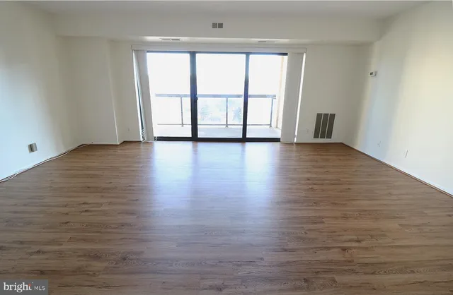 a view of an empty room with wooden floor and window