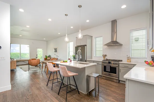 a kitchen with stainless steel appliances a stove a sink a oven a dining table and chairs with wooden floor