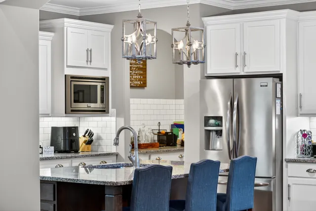 a kitchen with stainless steel appliances granite countertop a dining table chairs refrigerator and sink
