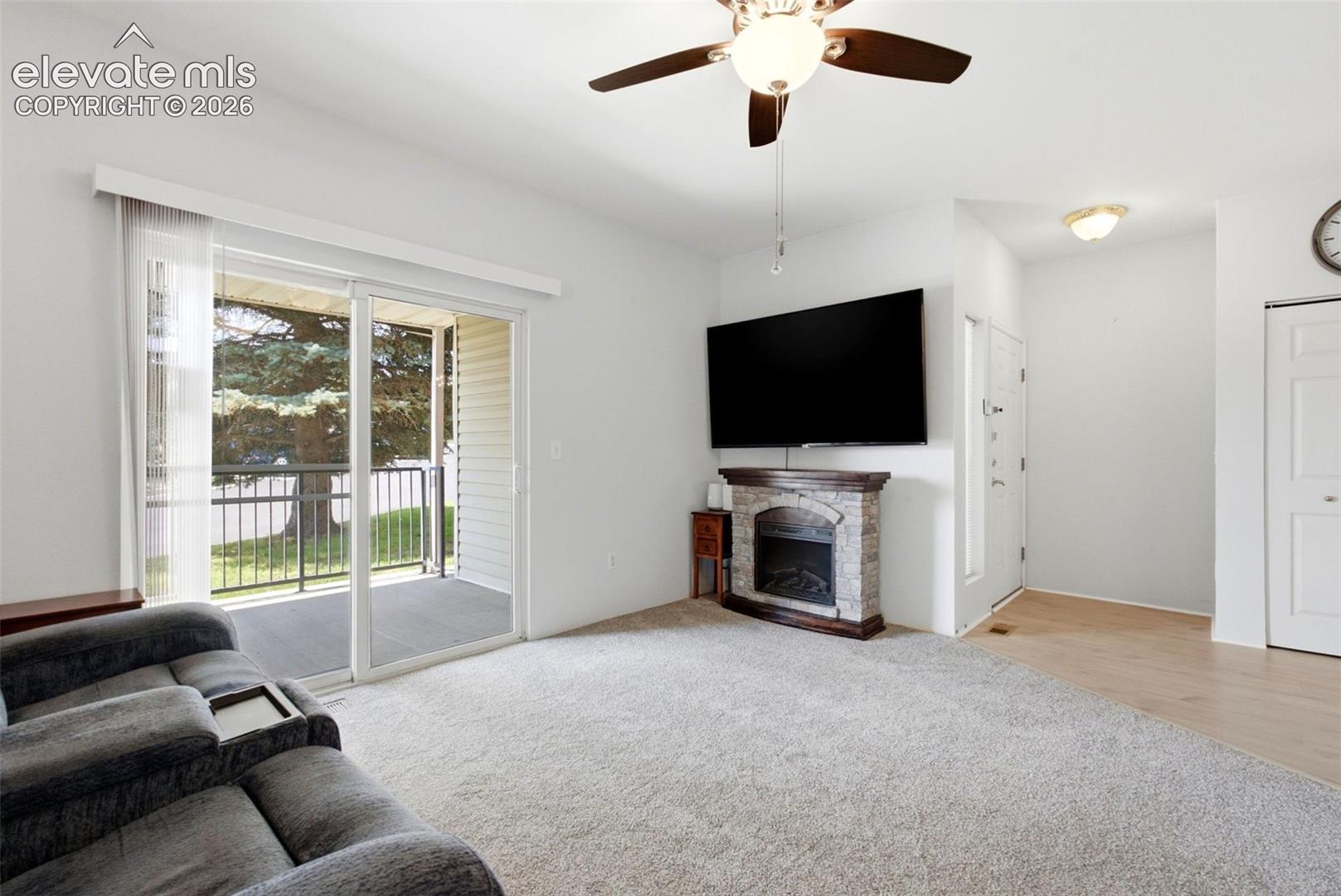 2002 Legacy Ridge View, Unit 107 Colorado Springs, CO 80910 - Photo 12 of 25 Carpeted living area with a ceiling fan, sliding glass door to a balcony, and a corner fireplace with a stone surround