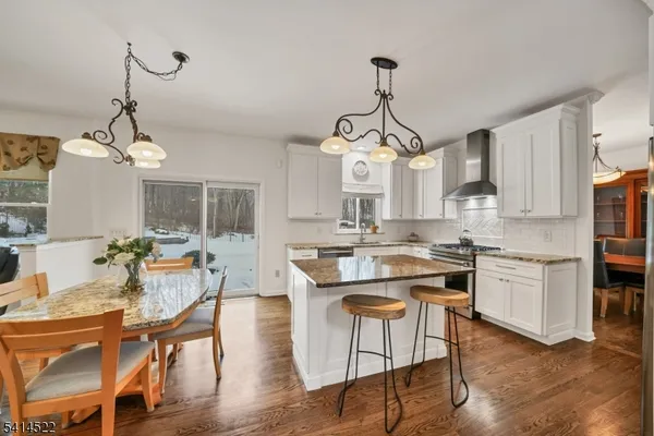 a very nice looking kitchen with granite countertop a stove a sink a dining table and chairs with wooden floor