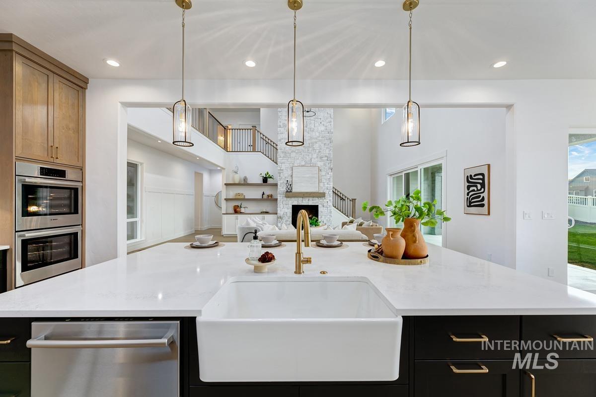 13339 North Hazel Grouse Way Boise, ID 83714 - Photo 9 of 50 Kitchen featuring dark cabinetry, stainless steel appliances, light stone countertops, pendant lighting, and a large fireplace