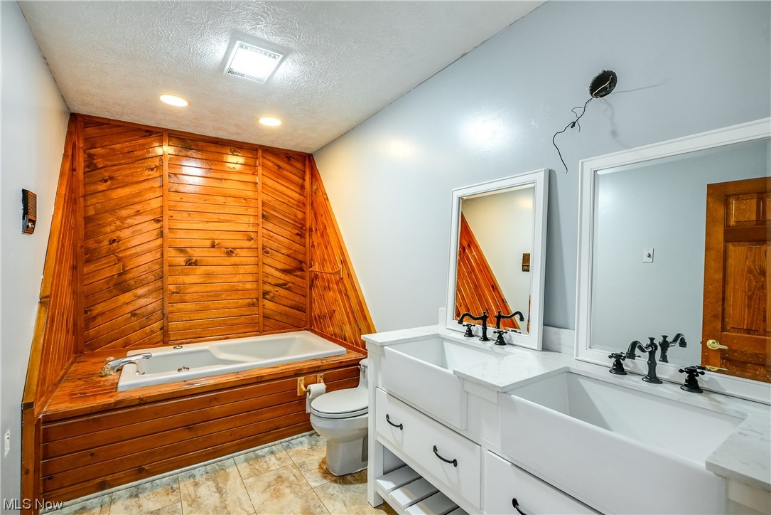 13920 Kneisel Road Vermilion, OH 44089 - Photo 20 of 35 Bathroom with vanity, a tub, toilet, a textured ceiling, and wood walls