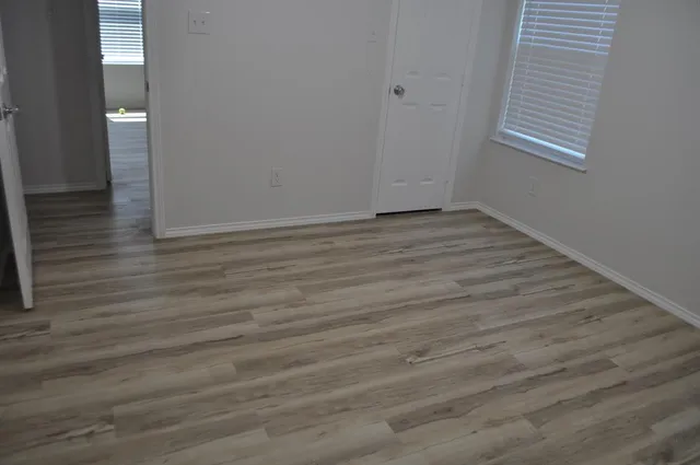 a view of an empty room with wooden floor and a window