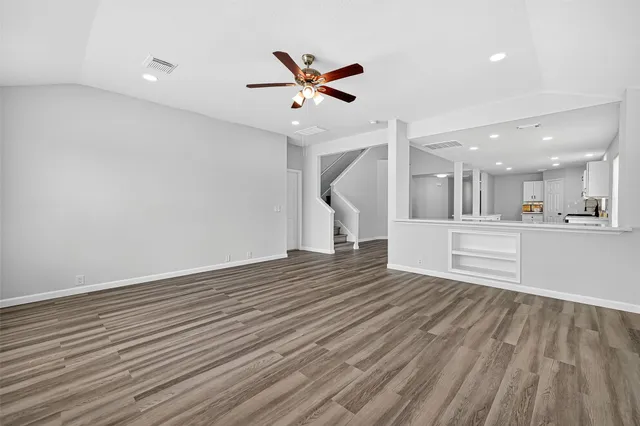 a view of an empty room with wooden floor and a ceiling fan