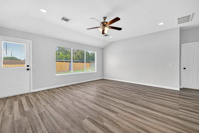 an empty room with wooden floor chandelier fan and windows